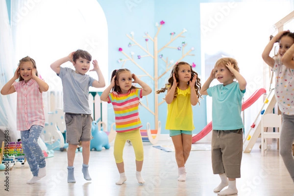 Fototapeta Happy kids having fun dancing indoors in a sunny room at day care or entertainment center