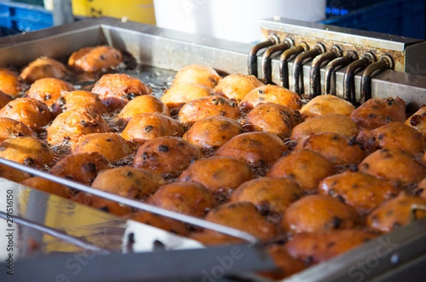 Fototapeta Close up of oliebollen with currants that are baking in a professional frying pan.
