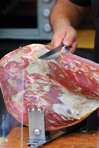 Fototapeta cook cuts some slices of seasoned ham with the meat knife
