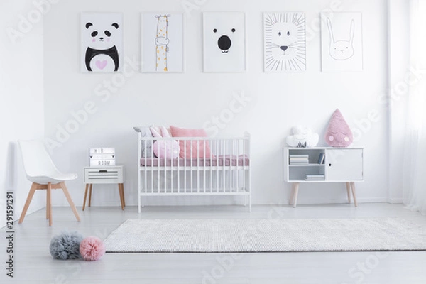 Fototapeta Pink cushions in cradle and chair in white child's room interior with posters and carpet. Real photo