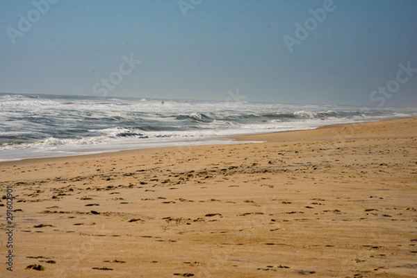 Fototapeta View of Footprints along empty beach around dusk with atlantic ocean waves