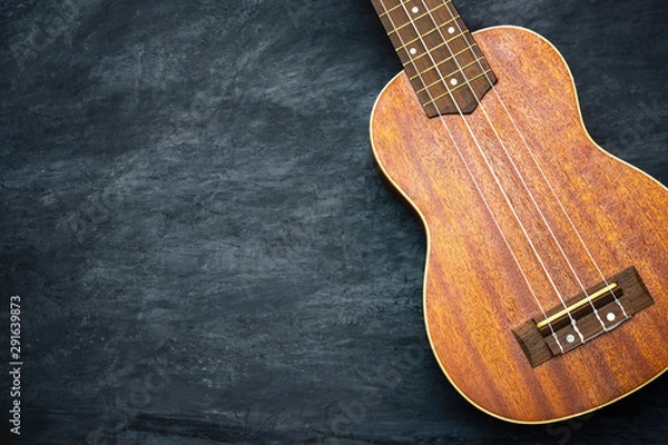 Fototapeta Ukulele on black cement background. Body and bridge of ukulele parts. Copy space for text. Concept of Hawaiian musical instruments and music lovers.