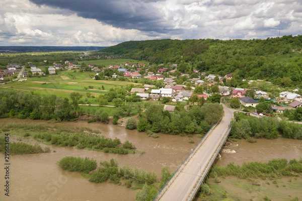 Fototapeta Aerial view of town or village with rows of buildings and curvy streets between green fields in summer. Countryside landscape from above.
