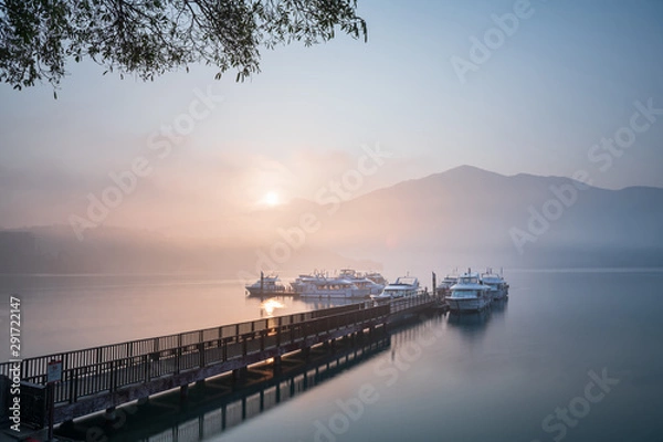 Fototapeta Beautiful tranquil landscape at Sun Moon lake in Nantao, Taiwan. Pier with boats and background of foggy mountains. Concept of peaceful, traanquility of nature.