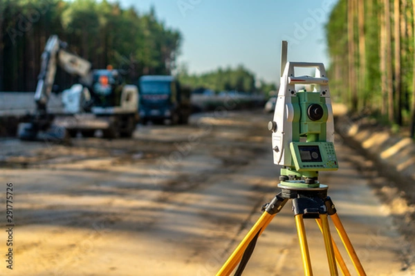 Fototapeta Surveyor engineer with equipment (theodolite or total positioning station) on the construction site of the road or building with construction machinery background