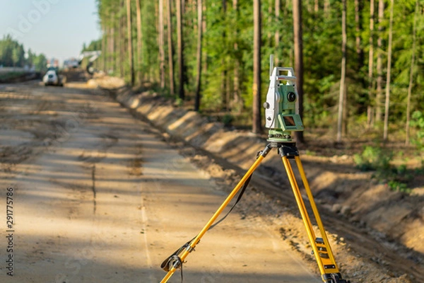 Fototapeta Surveyor engineer with equipment (theodolite or total positioning station) on the construction site of the road or building with construction machinery background