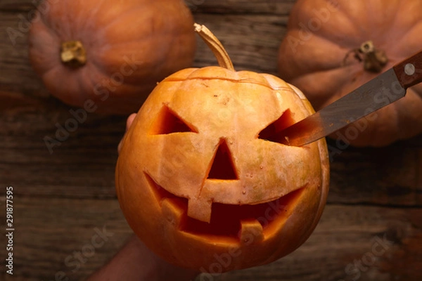 Fototapeta halloween, decoration and holidays concept - close up of hands with knife carving pumpkin or jack-o-lantern at home