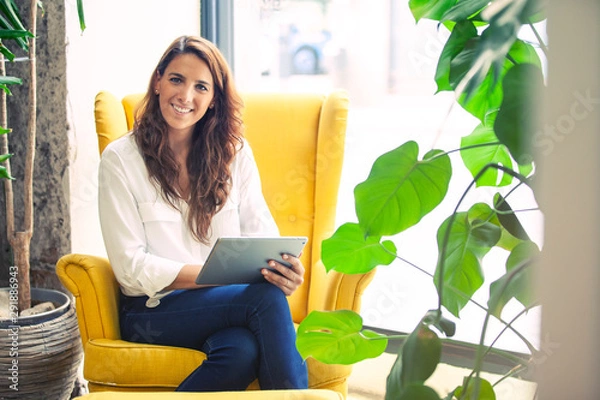 Fototapeta Portrait of a successful startup founder in the couch of her office, holding a tablet device. 