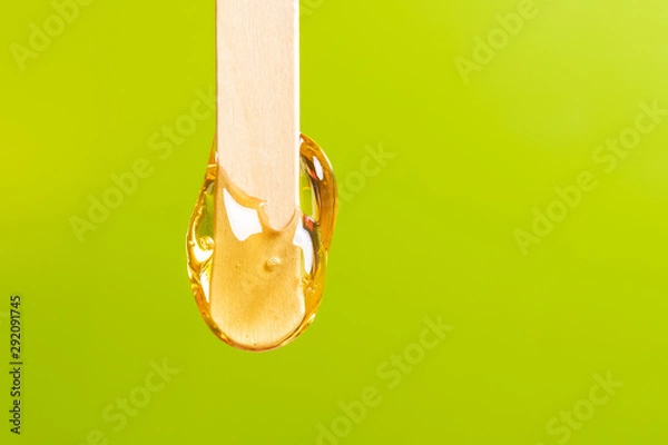 Fototapeta depilation and beauty concept - sugar paste or honey wax for hair removing spatula with wooden framing sticks on a bright green background