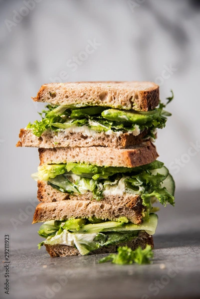 Fototapeta Three sandwiches on top of each other. Layered rustic breads with avocado and fresh salad on grey background.