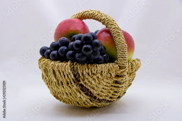 Fototapeta Apples and grapes in a basket on a white background.
