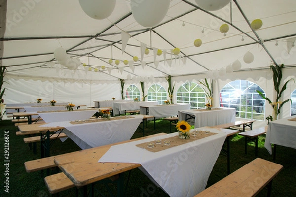 Fototapeta Arrangement dinner in a tent with wooden tables and benches. Decorated with sunflowers, candles and balloons.