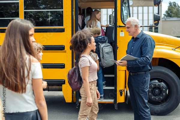 Fototapeta Classmates going into school bus while driver checking attendance concentrated joyful