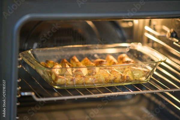 Fototapeta ready baked potato slices with spices lie in glass dish in the oven.