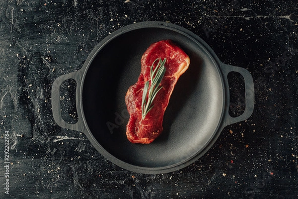 Obraz Raw beefsteak on a frying pan with a rosemary, top view, flat lay, copyspace.