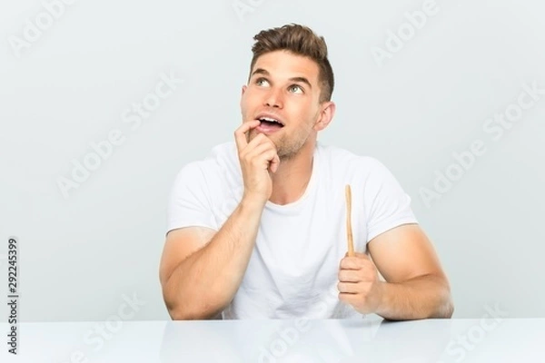 Obraz Young man holding a toothbrush relaxed thinking about something looking at a copy space.