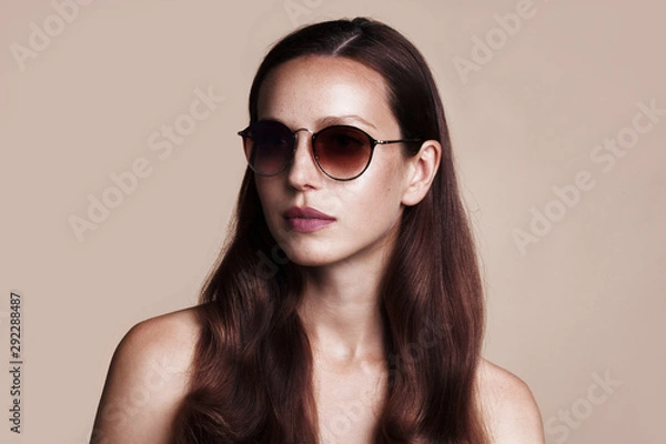 Fototapeta Bliska portret całkiem młoda kobieta w okularach na szarym tle. Modelka pozowanie z okularami przeciwsłonecznymi.