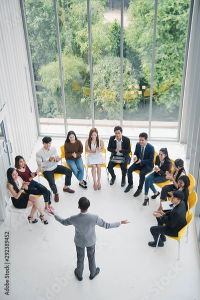 Fototapeta Seminar group, Successful young Asian business man and woman, the man speaker presenting to employees, business coach giving presentation to clients in meeting room, team leader reporting about work.