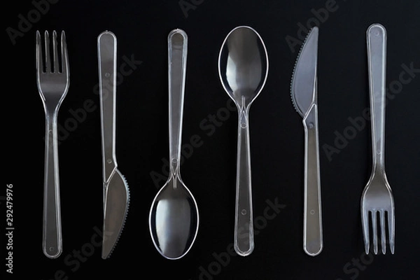 Fototapeta Transparent plastic spoons, knives and forks on black background. Clear disposable cutlery set. Top view