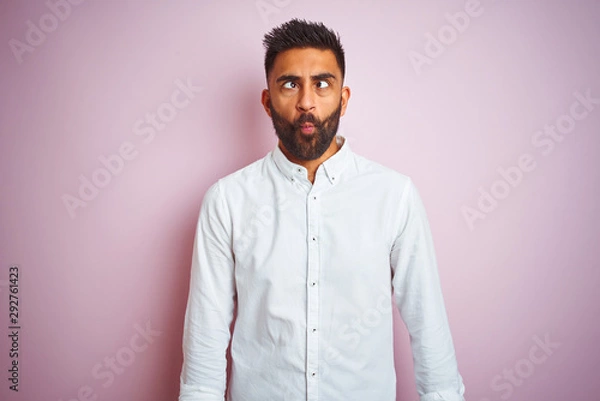 Fototapeta Young indian businessman wearing elegant shirt standing over isolated pink background making fish face with lips, crazy and comical gesture. Funny expression.