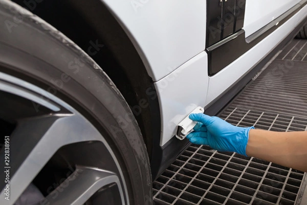 Obraz The process of applying a nano-ceramic coating on the white car's fender arch by a male worker with a sponge to protect the paint in detailing workshop. Auto service industry.