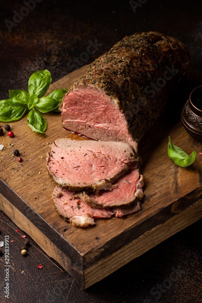 Obraz Juicy roast beef with spices sliced on a cutting Board, delicious meat, traditional food. On dark background