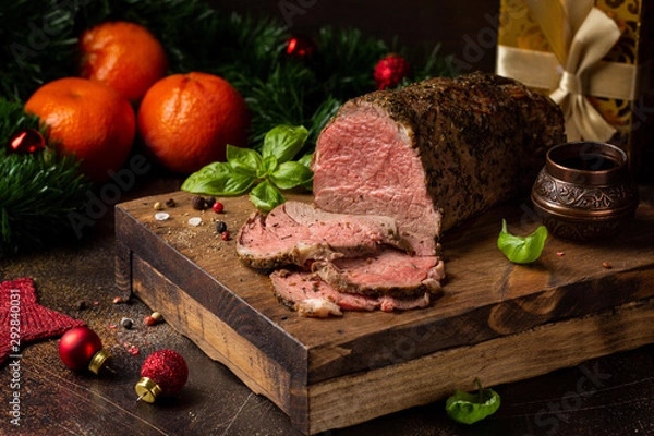 Obraz Juicy roast beef with spices sliced on cutting Board, delicious meat, traditional food. Christmas holidays, new year, menu on dark background