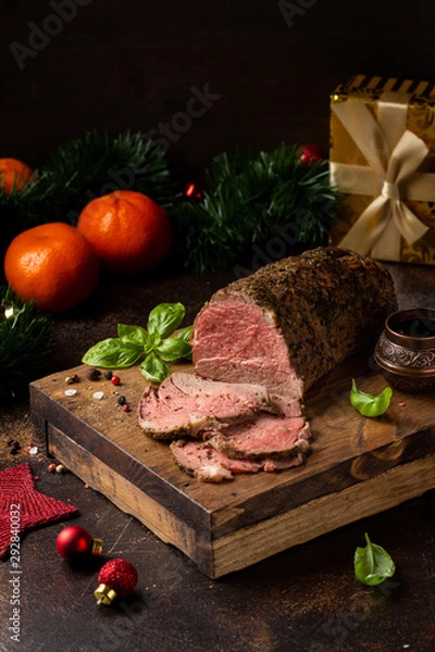 Obraz Juicy roast beef with spices sliced on cutting Board, delicious meat, traditional food. Christmas holidays, new year, menu on dark background