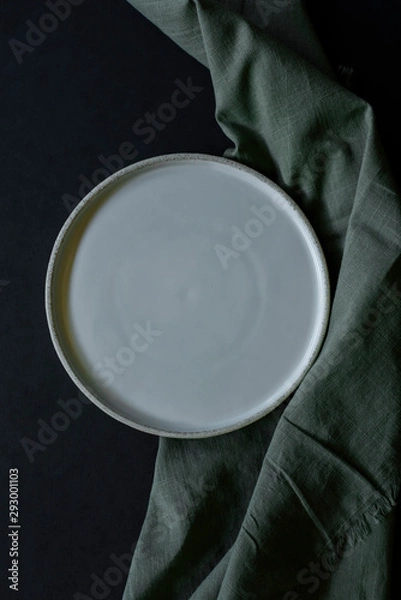 Obraz white handmade plate with green fabric napkin on dark background, handmade pottery plate on black table, empty plate, mockup, copyspace, empty space