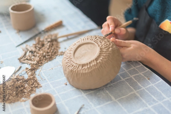 Fototapeta Ceramic girl making clay dishes in a workshop, a stage of drawing a pattern