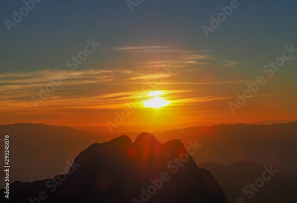 Fototapeta The high mountains of Chiang Dao in Chiang Mai, Thailand, as the sun sets behind the mountain peaks, the clouds in the sky are golden, red, orange, and yellow.