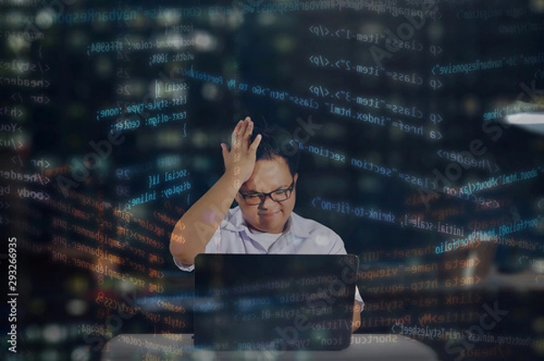 Obraz Young male programmer with glasses getting stressed out while coding for an HTML website or for web development. Shot behind office window at night with HTML codes surrounding the programmer. 