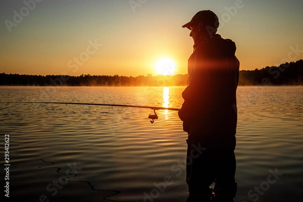 Fototapeta Male fisherman at dawn on the lake catches a fishing rod. Fishing hobby vacation concept. Copy space.