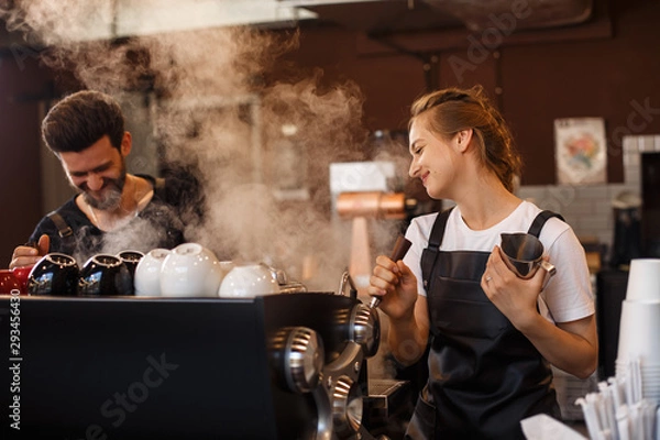 Obraz Dwóch młodych uśmiechniętych baristów w pracy. Profesjonalny zespół baristów parzy kawę za pomocą ekspresu do kawy w kawiarni. Szczęśliwy młody mężczyzna i kobieta rozwija własny biznes kawowy. Koncepcja kawiarni.