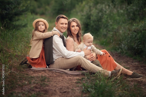 Obraz family with two children sitting on the ground in the forest and smiling at the camera