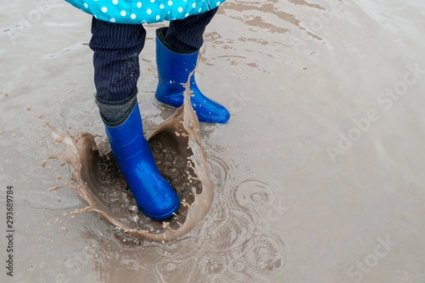 Fototapeta the child is dressed in rubber boots strongly stomps on a puddle. drops of dirty water spray everywhere.