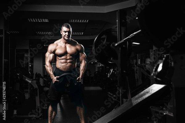 Fototapeta Muscular man bodybuilder training in gym and posing. Fit muscle guy workout with weights and barbell