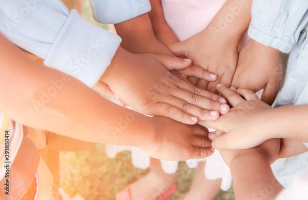 Fototapeta Group of ethnically diverse kids students putting their hands together. Teamwork, cooperation, learning, and education concept.