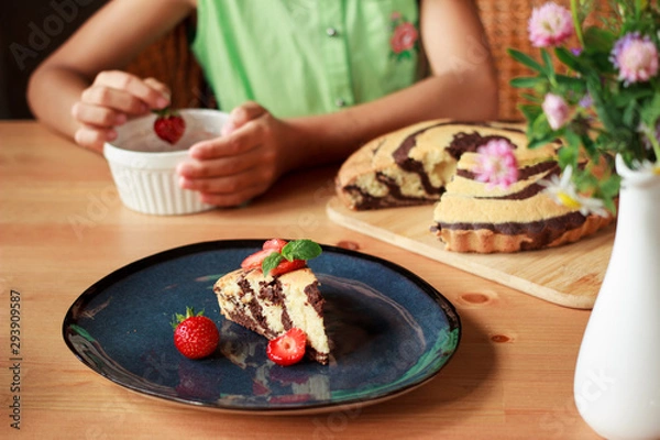 Fototapeta Homemade chocolate zebra cake with strawberries on dark blue plate on wooden table