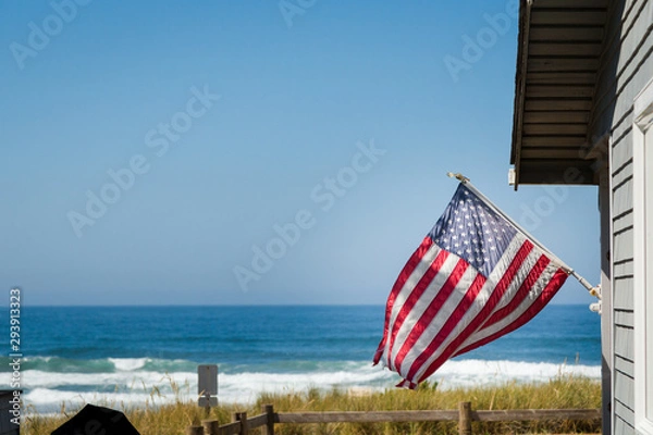 Fototapeta A beautiful oceanfront property with a classic American flag on the side of it with the coastline in the background.