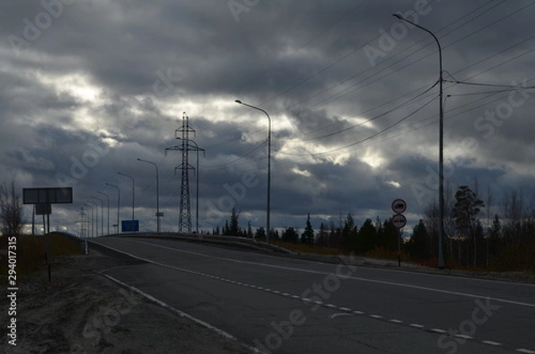 Fototapeta The road out of town into the distance, against the sky and clouds.