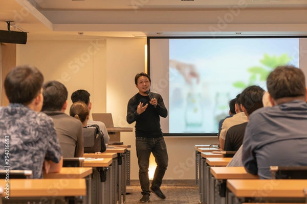 Fototapeta Asian Speaker is speaking on the stage over the presentation screen in the education seminar