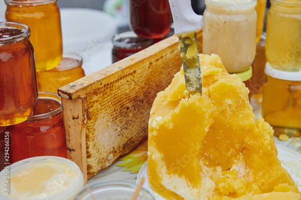Fototapeta A lot of honey products at the market. Jars with different varieties of honey. The knife sticks out of honey. Honey farm products.