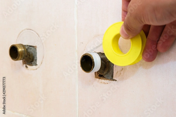 Fototapeta The plumber puts Teflon seam FUM tape on the thread before installing the faucet tap. Close up