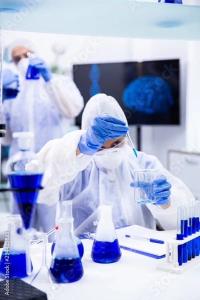 Fototapeta Chemist holding a pipette with a blue liquid trying to make an experiment