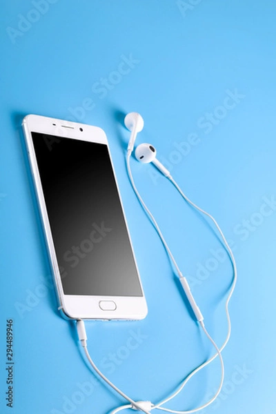 Fototapeta  Mobile headphones and a mobile phone of white color on a blue background in light colors with a place for text.