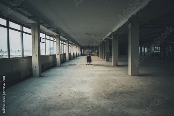 Fototapeta Man sitting in front of a large window in an empty hall of an abandoned building