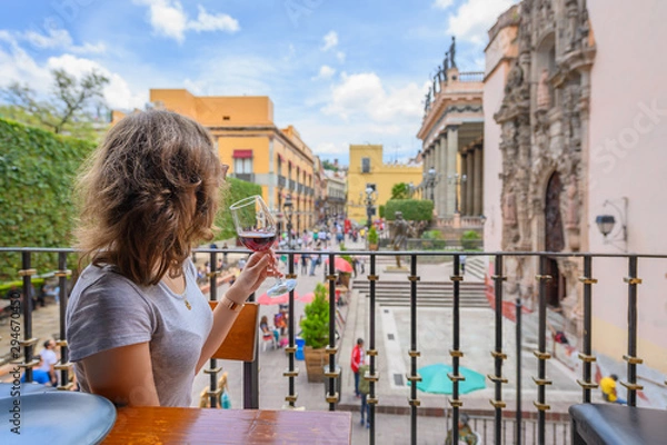 Obraz Woman on a restaurant balcony watching the colorful city of Guanajuato having a glass of red wine