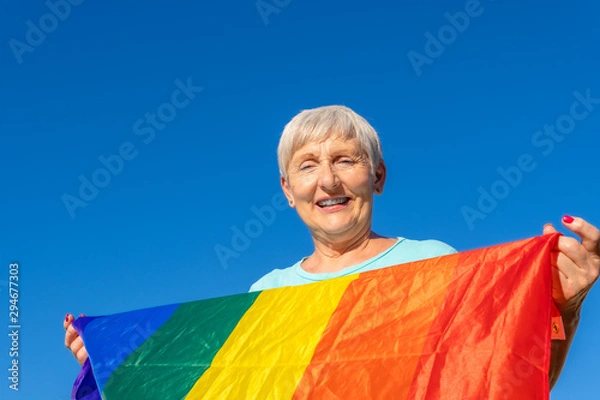 Obraz smiling senior woman with lgbt flag on blue background