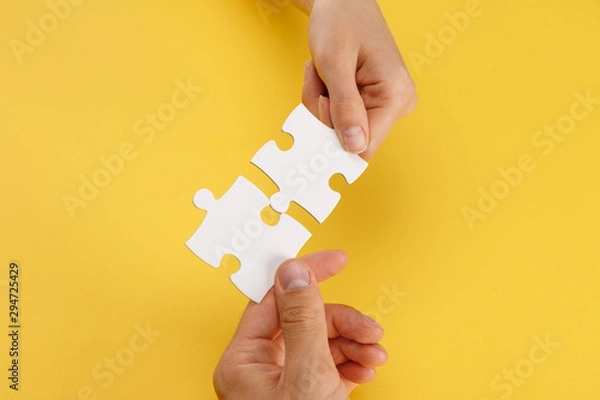 Fototapeta cropped view of woman and man matching pieces of white puzzle on yellow background